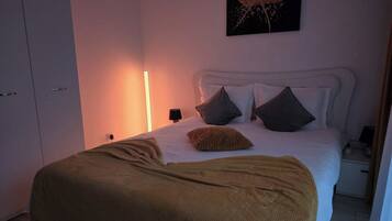 A bedroom with a bed, pillows, a bedside table, a lamp, a wardrobe, and a painting on the wall.