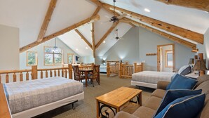 A spacious loft bedroom with a high ceiling, wooden beams, a large bed, a sofa, a dining table, and a ceiling fan.