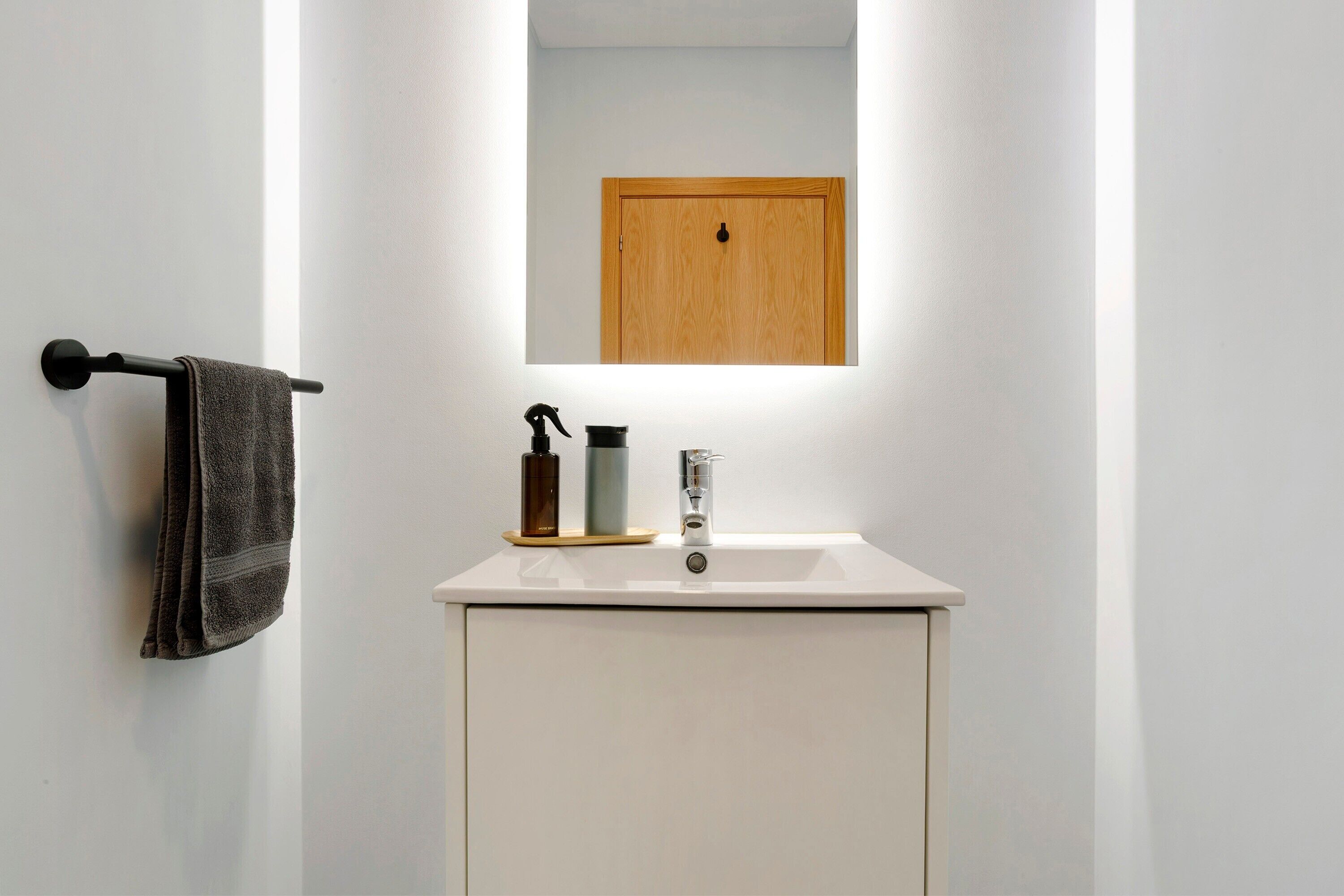 A bathroom with a white sink, a towel rack, a mirror, and a wooden door.