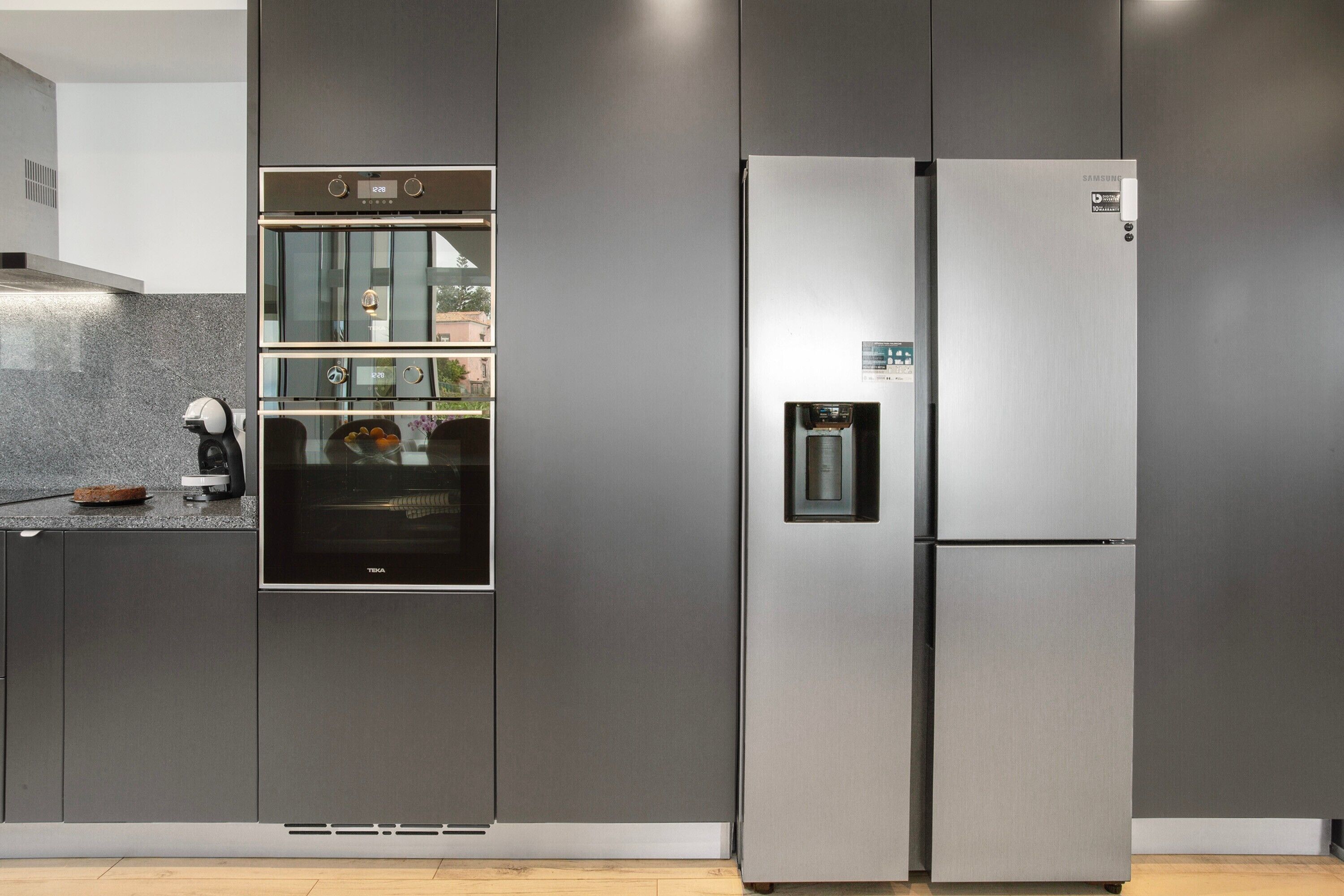 A modern kitchen with a built-in oven, a stainless steel refrigerator, and a water dispenser.