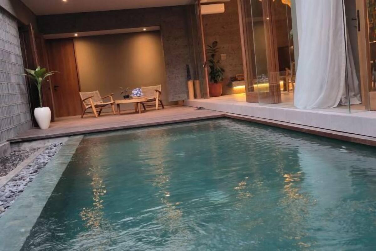 Una piscina con zona de estar, una planta en maceta y una puerta corredera de vidrio.