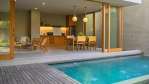 Una cocina moderna con armarios de madera, un área de comedor con sillas y un espacio de descanso junto a la piscina.
