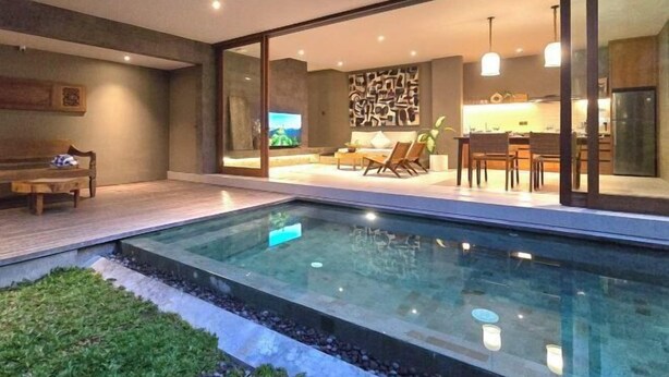 Un interior moderno con piscina acristalada, comedor y cocina a la vista a través del vidrio.