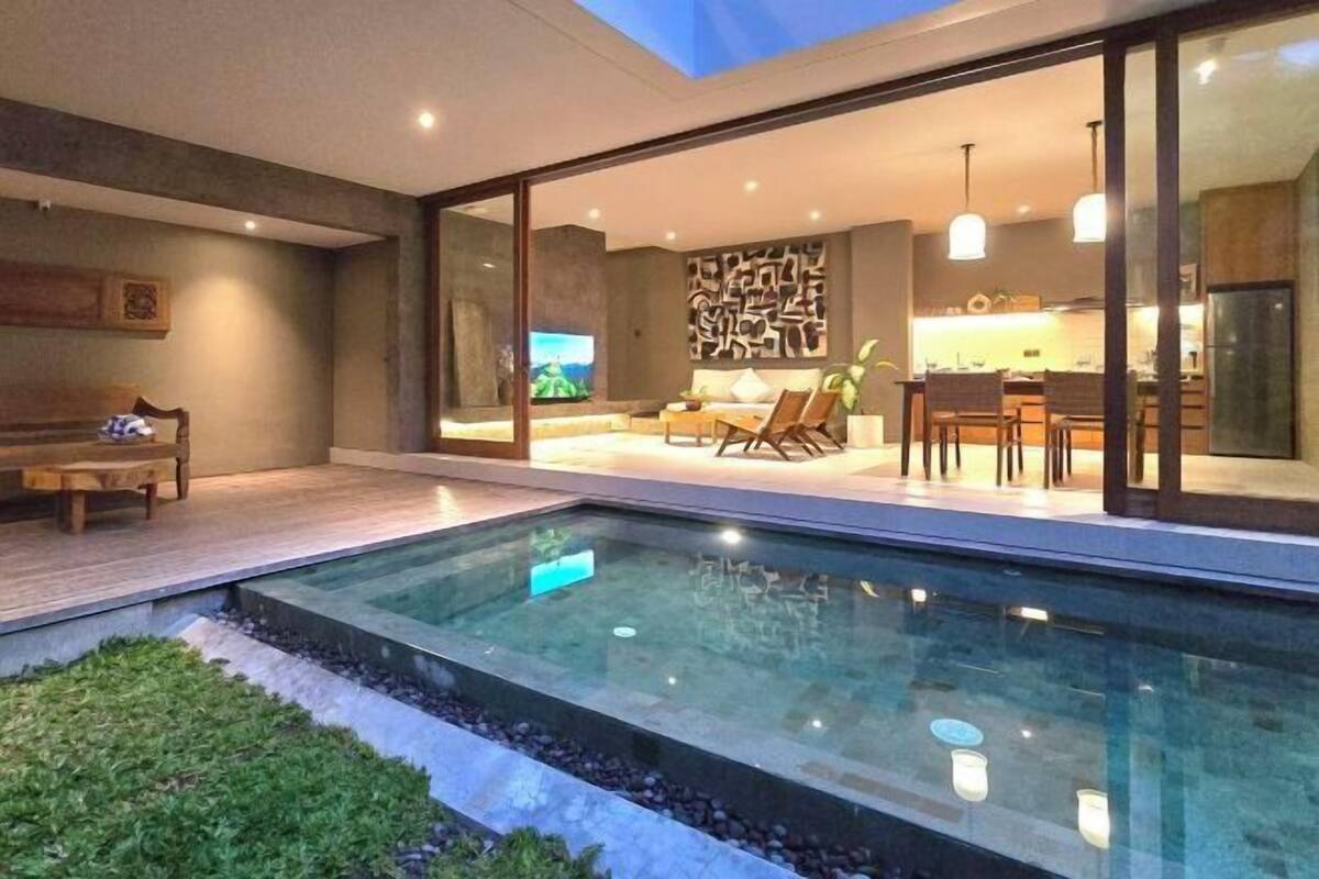 Un interior moderno con piscina acristalada, comedor y cocina a la vista a través del vidrio.