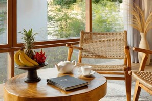 A wicker chair, a table with a book, a teapot, and a fruit bowl. - Pulang Villas Pererenan (Bali)