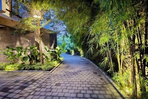 A paved pathway flanked by lush greenery and bamboo plants, leading towards a building. - Pulang Villas Pererenan (Bali)