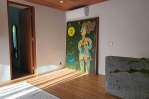 Een kamer met houten vloer, een schilderij aan de muur en een deur naar een andere kamer.