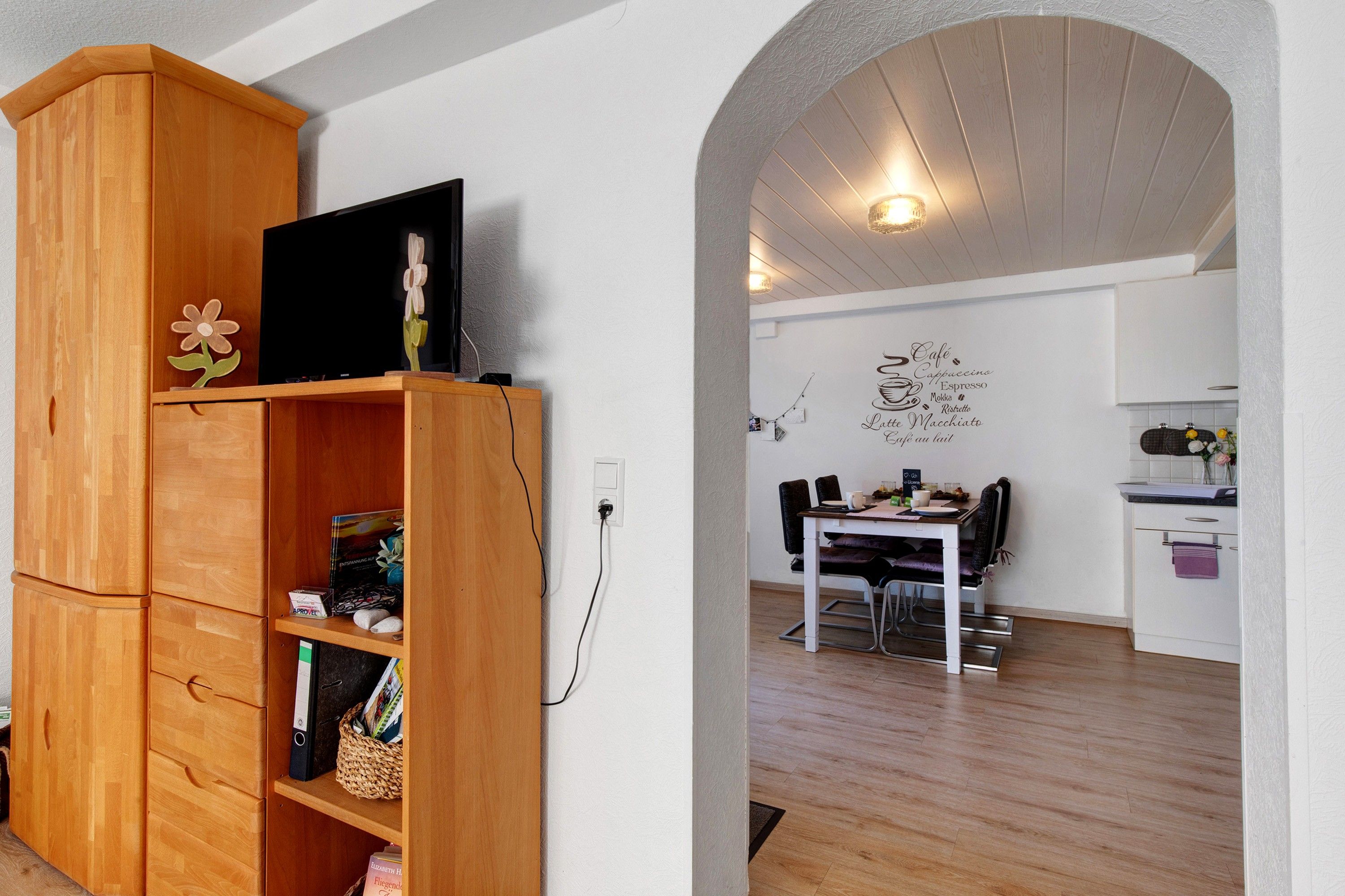 A wooden cabinet with a flat-screen TV, a wall-mounted light fixture, and a dining area with a table and chairs.