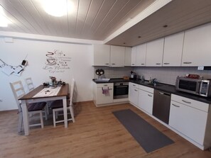 A modern kitchen with white cabinets, a dining table with chairs, a coffee station, and a microwave.