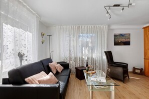 A modern living room with a black leather sofa, a glass coffee table, a black armchair, and a painting on the wall.