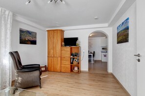 Un salón amplio con un sillón de cuero, un armario de madera y un televisor de pantalla plana.
