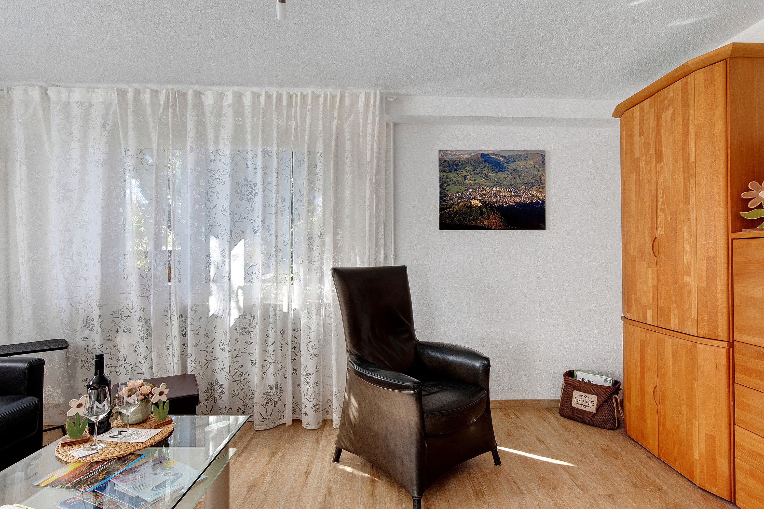 A living room with a leather chair, a glass coffee table, a wooden cabinet, and a painting on the wall.
