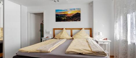 Una cama bien tendida con un cabecero, una mesita de noche con una lámpara y un cuadro de un paisaje en la pared.