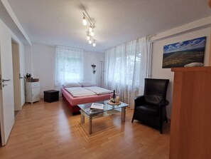 A room with a bed, a glass coffee table, a black leather chair, a wooden cabinet, and a painting on the wall.