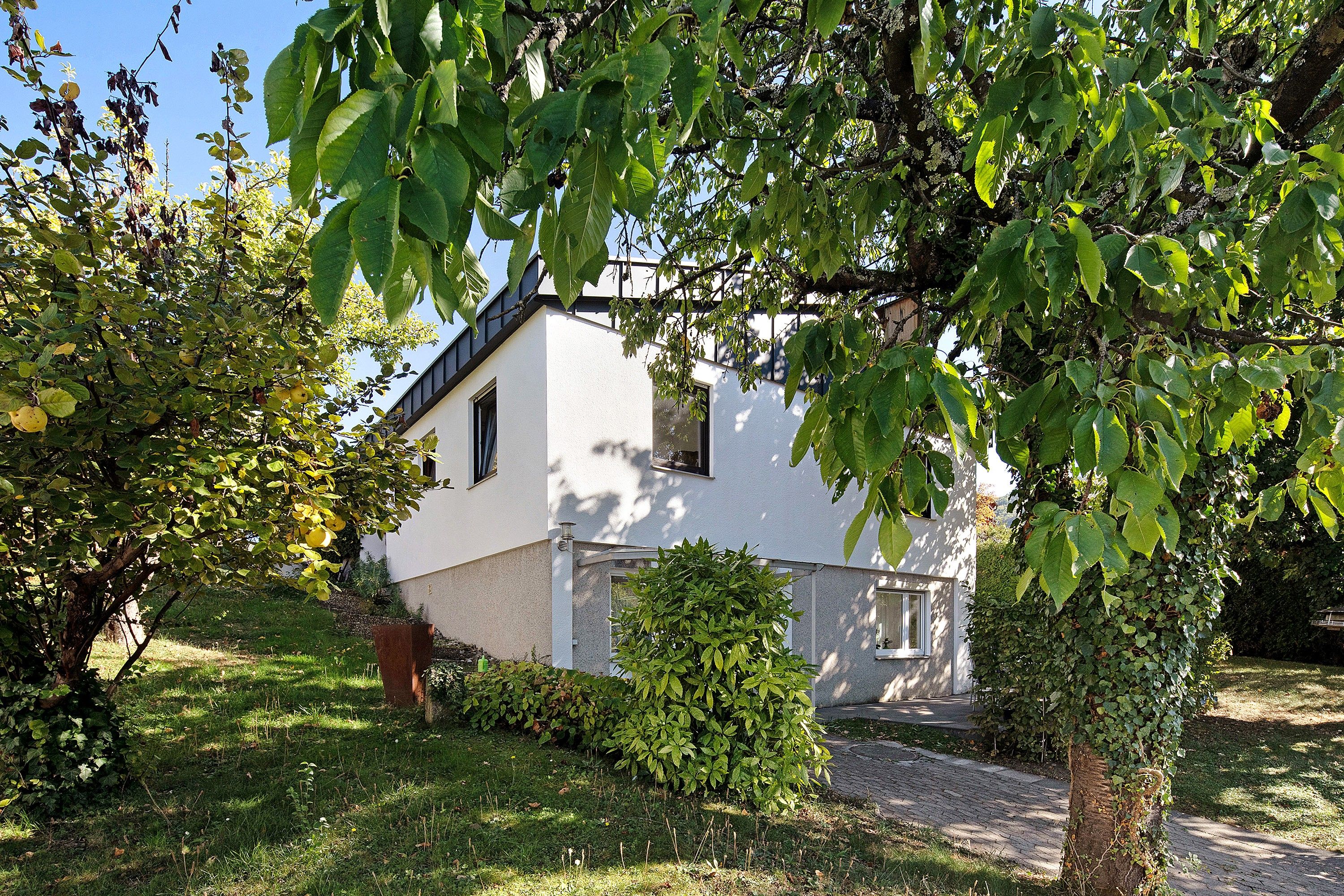 A white house with a sloped roof, surrounded by lush greenery and a well-maintained lawn.