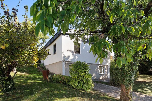 Une maison blanche avec un toit en pente, entourée d’une végétation luxuriante et d’une pelouse bien entretenue.