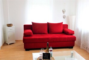 A red sofa, a small white cabinet, a glass table with a bottle, glasses, and a menu.