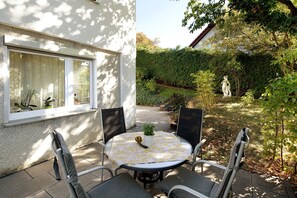 An outdoor patio with a round table and four chairs, a potted plant, and a statue in the background.