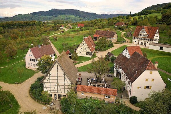 A village with traditional half-timbered houses, a central courtyard, and surrounding green fields.