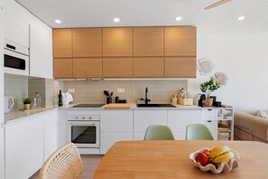 Une cuisine moderne avec des meubles blancs, un plan de travail en bois et un coin repas comprenant une table et des chaises.