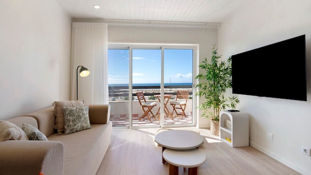 Ein modernes Wohnzimmer mit Sofa, rundem Tisch, Flachbildfernseher und Balkon mit Blick.