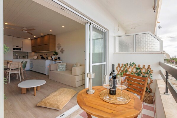 A balcony with a table, two chairs, a bottle of wine, and a glass.