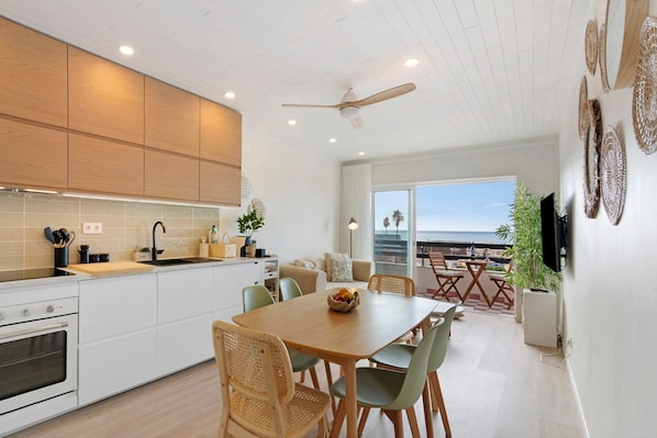 Une cuisine moderne avec des meubles blancs, un coin repas avec une table et des chaises en bois, et un balcon avec vue.