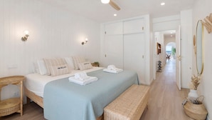 Ein Schlafzimmer mit Bett, Deckenventilator, Wandleuchten, Spiegel und einem Flur zu einem anderen Raum.