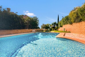 A swimming pool with clear blue water, surrounded by brick walls and greenery.