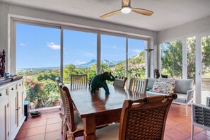 A dining area with a view of a mountainous landscape, a ceiling fan, and a dining table with chairs.