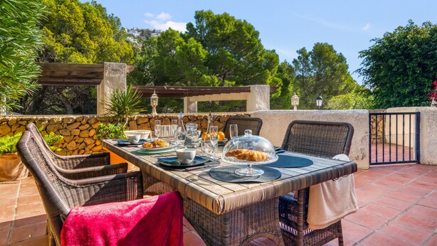 An outdoor dining area with wicker furniture, a stone wall, and a view of trees and hills. - Holiday Home 'Oceanview House' with Sea View, Wi-Fi and Air Conditioning (Altea)
