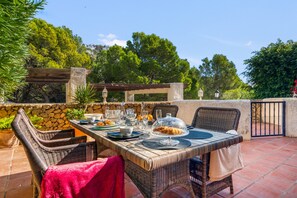 Un espacio de comedor al aire libre con mobiliario de mimbre, una pared de piedra y vistas a árboles y colinas.