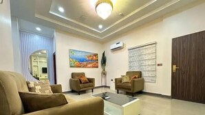 A modern living room with a sofa, two armchairs, a coffee table, and a painting on the wall. - Haussefour Apartment (Abuja)