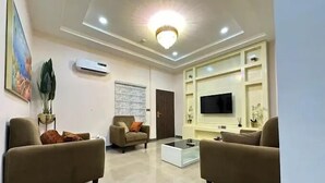 A modern living room with two sofas, a coffee table, a TV, and a chandelier. - Haussefour Apartment (Abuja)