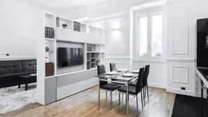 A modern living room with a built-in TV, a dining area with a table and chairs, and a staircase leading to another level. - Acquileia - Stylish loft  steps from Corso Magenta (Milano)