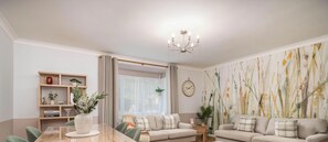 A modern living room with a dining table, sofas, a chandelier, and a large abstract painting on the wall.