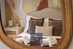 A neatly made bed with a headboard, a bedside table with a lamp, and a mirror reflecting the room.