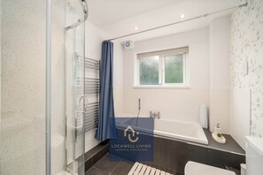 Ein modernes Badezimmer mit Duschkabine aus Glas, einer Badewanne und einem Fenster.