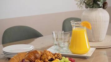 Une table mise pour le petit-déjeuner avec des croissants, des fruits, un pichet de jus d’orange et un vase rempli de verdure.
