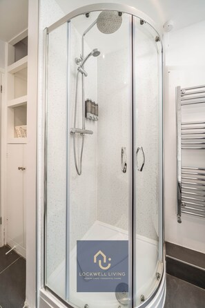 A modern shower enclosure with a glass door, a handheld showerhead, and a wall-mounted faucet.