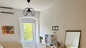 A modern living room with a white sofa, a dining table with chairs, a large window, and a ceiling fan.