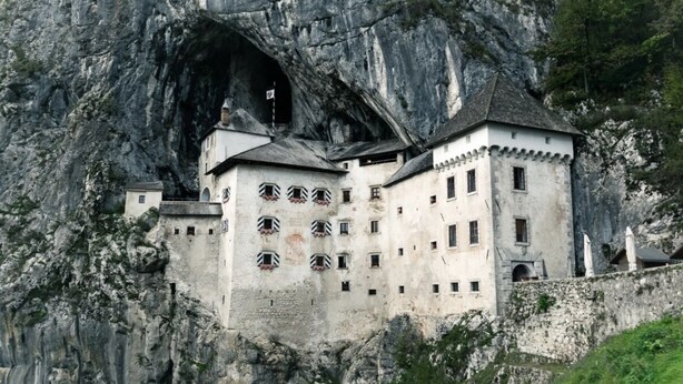 A castle built into a cliffside with multiple windows and a flag.