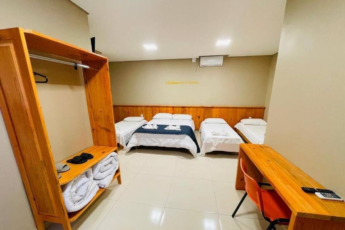 A hotel room with a wooden wardrobe, two single beds, a desk with a chair, and a small table.