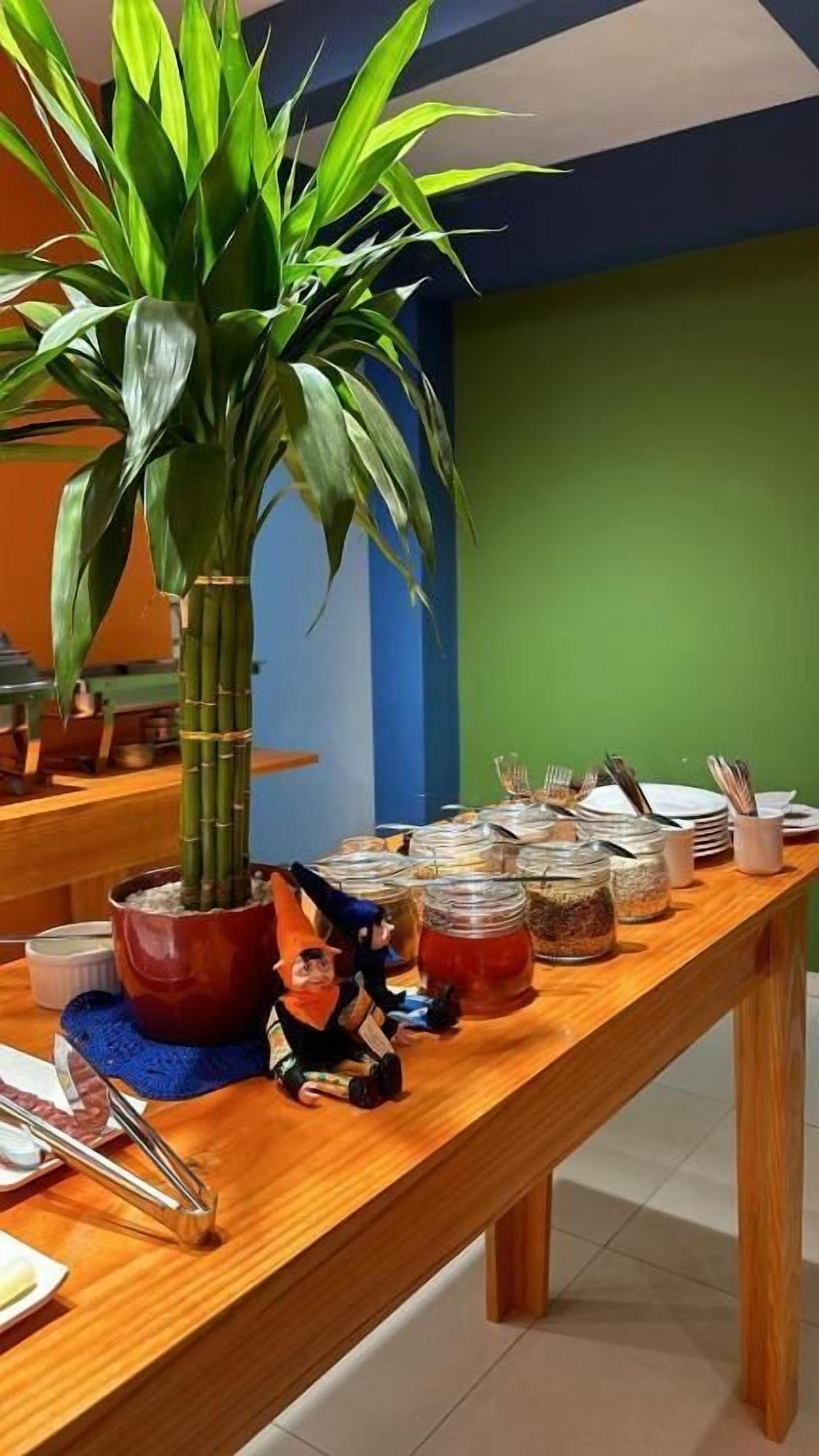 Une table à manger ornée d’une grande plante verte, de différents récipients contenant de la nourriture et d’ustensiles.