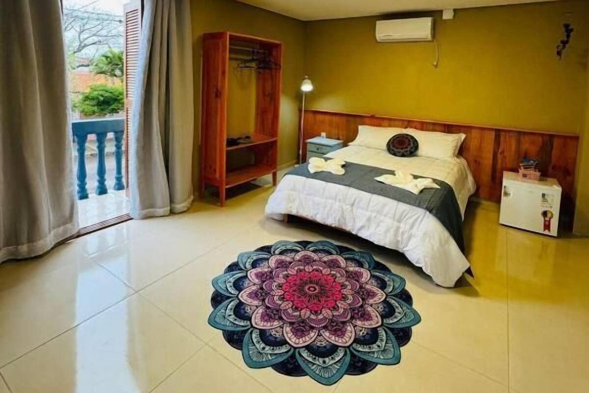 A bedroom with a bed, a wardrobe, a bedside table, a lamp, and a decorative rug.