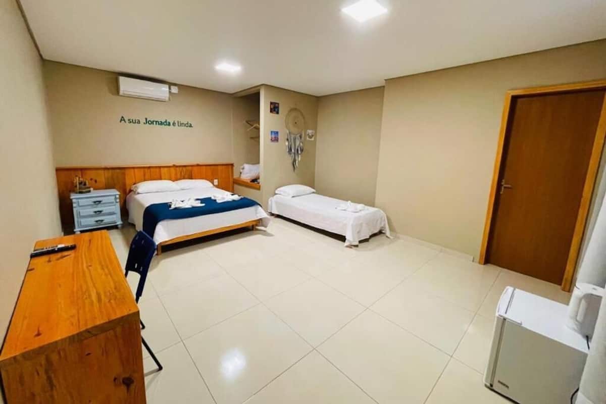 A hotel room with a bed, a desk, a chair, a wardrobe, and a small kitchenette.