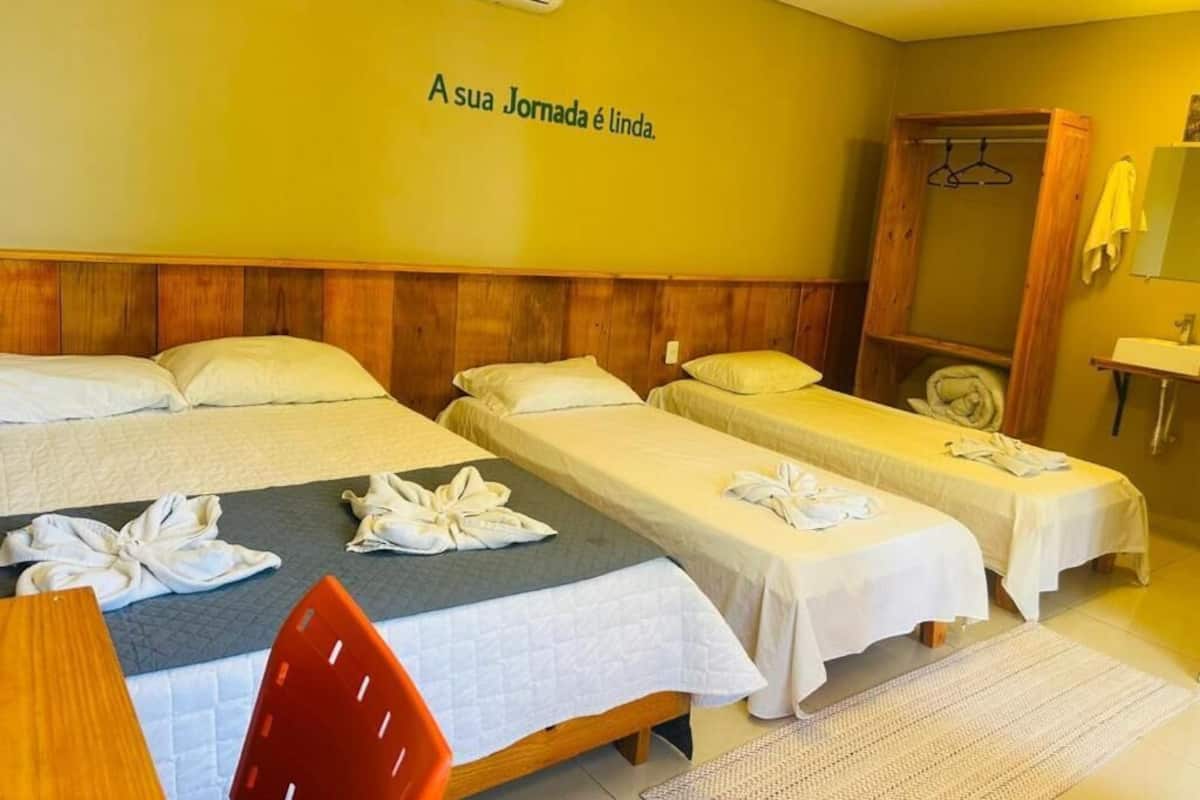 A hotel room with two beds, a wooden headboard, a wall-mounted air conditioner, a mirror, and a towel rack.