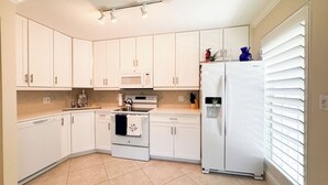 A modern kitchen with white cabinets, a built-in oven, a microwave, a refrigerator, and a water dispenser. - Ville De Marco M-1: Beautiful Condo in Olde Marco (Marco Island)