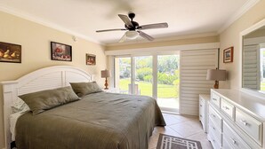 A bedroom with a bed, a ceiling fan, a sliding glass door to a garden, and a dresser. - Ville De Marco M-1: Beautiful Condo in Olde Marco (Marco Island)
