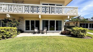 A two-story building with a balcony, large sliding glass doors, and a patio area with outdoor furniture. - Ville De Marco M-1: Beautiful Condo in Olde Marco (Marco Island)